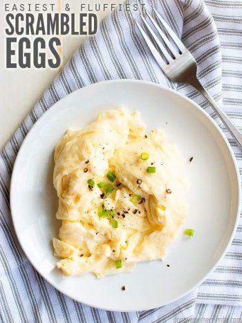 Fluffy scrambled eggs, garnished with green onions, on a round white plate, on a striped kitchen towel. Text overlay Easiest & Fluffiest Scrambled Eggs.