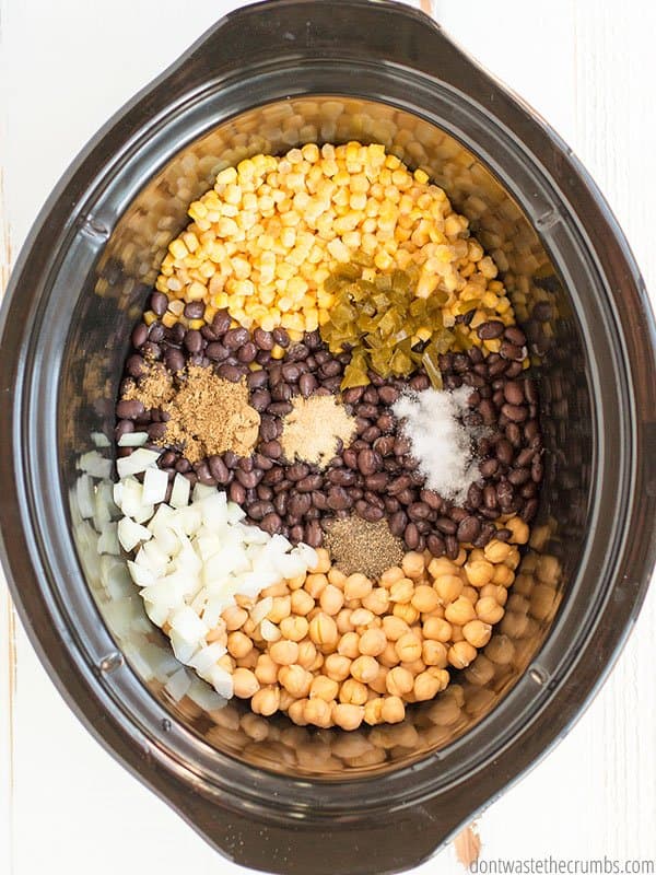Corn, spices, black beans, garbanzo beans are in a slow cooker pot.