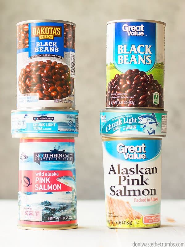 Canned black beans, canned tuna, and canned pink salmon from Walmart and ALDI, stacked in two piles.