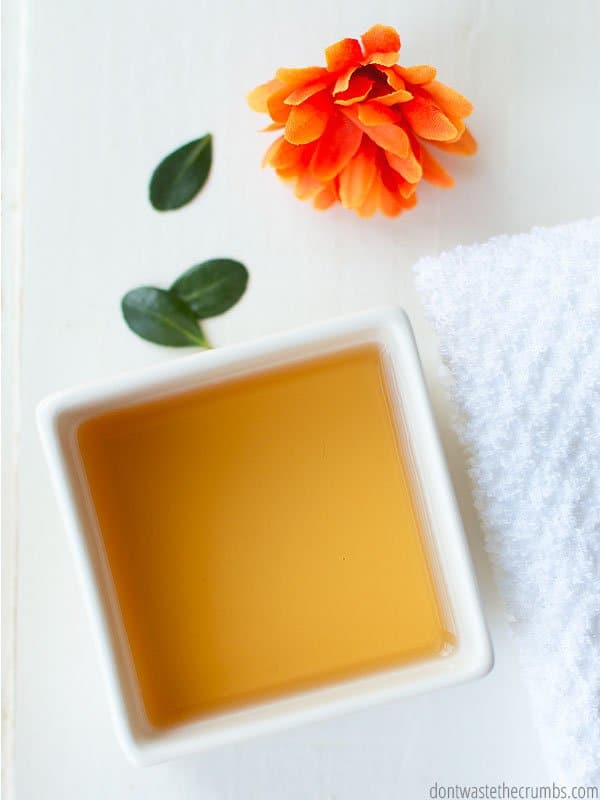 There is a small white square dish holding apple cider vinegar. This is an optional step for detoxing your armpits. An orange flower with green leaves decorate the image.