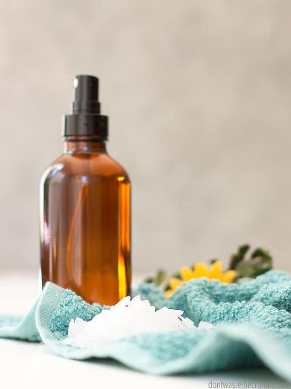 Glass amber spray bottle with magnesium oil on a towel. There are magnesium chloride flakes on the towel.