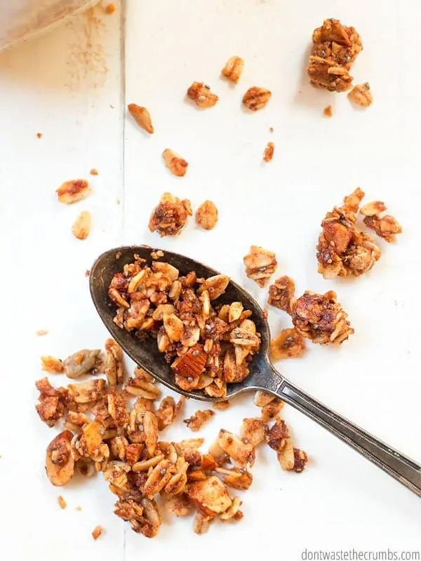 Up close view of cinnamon granola on a spoon and some granola is pictured in the background.