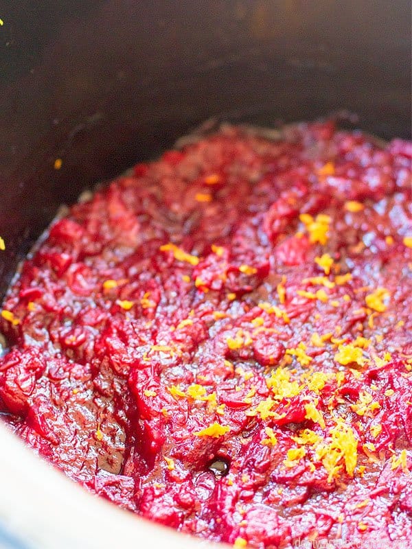 This cranberry sauce recipe is in a slow cooker pot with orange zest sprinkled throughout.