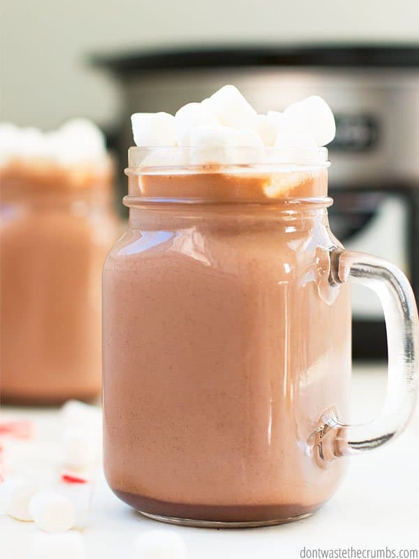 This crockpot hot chocolate is served and in a glass mason cup. Topped with homemade whipped cream, this makes the perfect treat for a cold night!