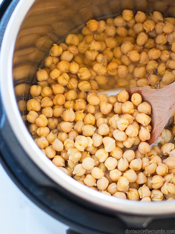 Instant Pot with freshly cooked garbanzo beans inside, scooped up with a wooden spoon.