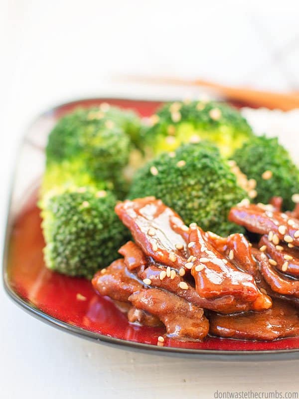 Close-up image of cooked sliced of beef and steamed broccoli on a plate, topped with sesame seeds.