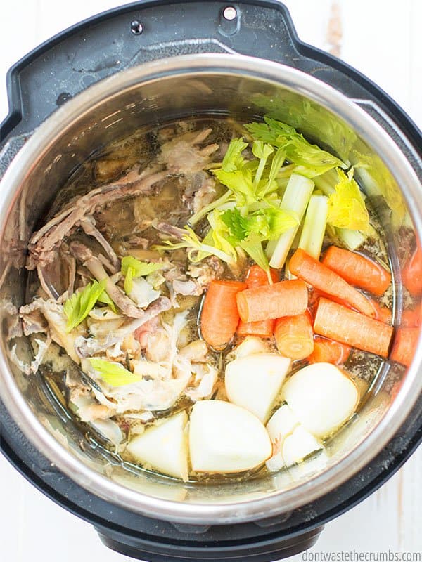 Chicken stock ingredients in the Instant Pot, including carrots, onion, celery, chicken bones, water, ready to cook for Freezer Cooking Day