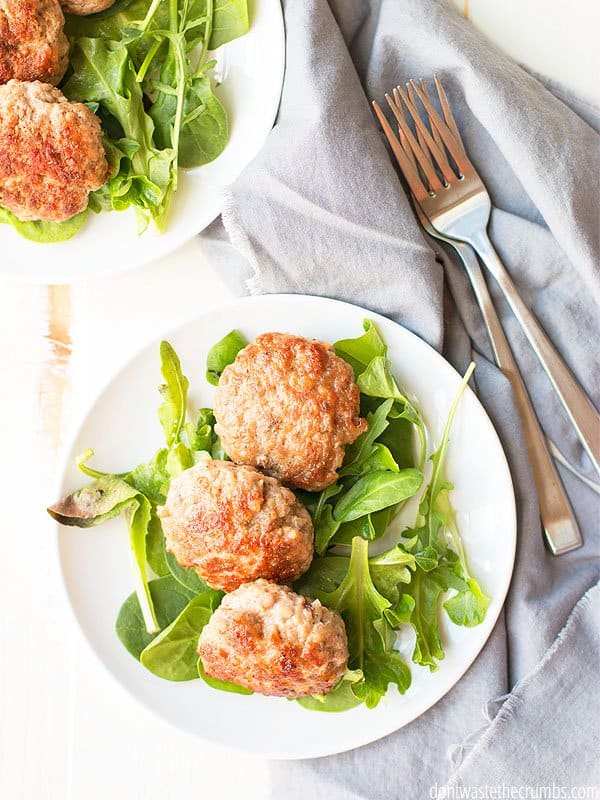 Turkey meatballs on a plate with fresh greens. There are two forks and a cloth napkin beneath the silverware.