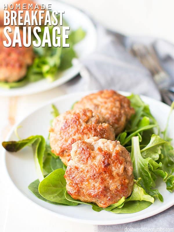 Two breakfast sausages on some greens on a plate. Text overlay reads Homemade Breakfast Sausage.