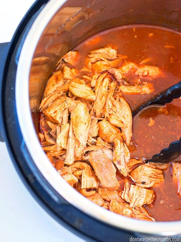 An Instant pot filled with BBQ sauce and shredded chicken. There is a set of tongs ready to serve the BBQ chicken.