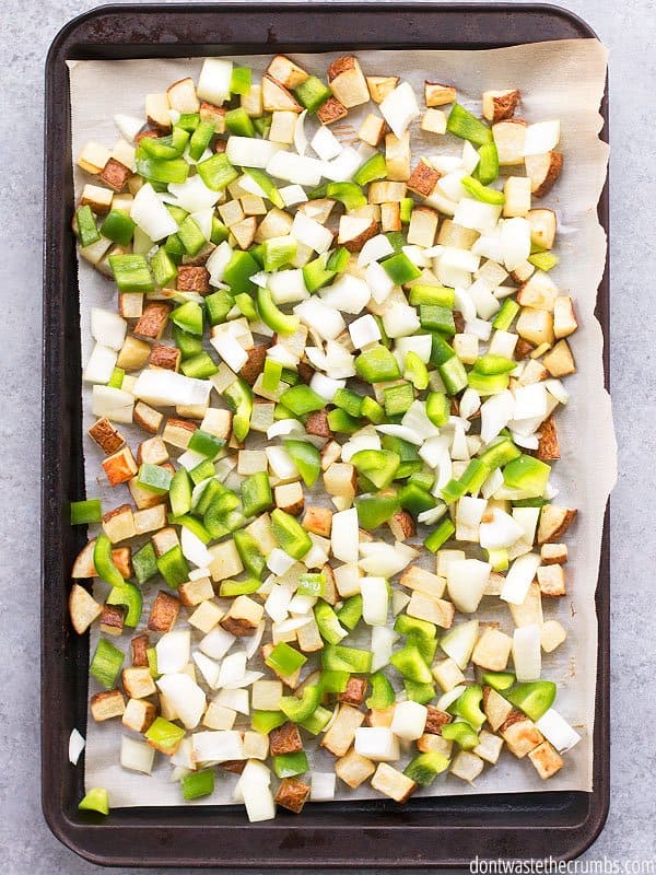 Homemade hash browns are diced and spread on a baking sheet with onions and green peppers. 