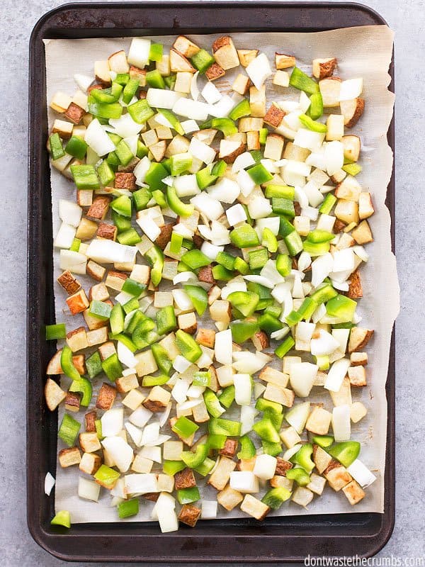 Homemade hash browns are diced and spread on a baking sheet with onions and green peppers.