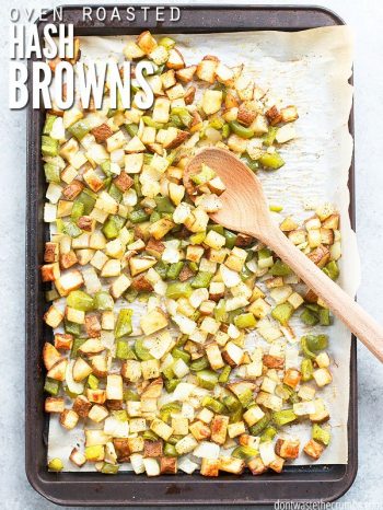 Large cooking sheet, with a parchment paper covering, filled with uncooked sliced potatoes, green peppers and white onions. Text overlay Oven Roasted Hash Browns.