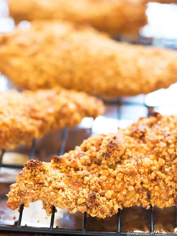 Four almond crusted chickens on a cooking rack on a foil lined baking sheet.