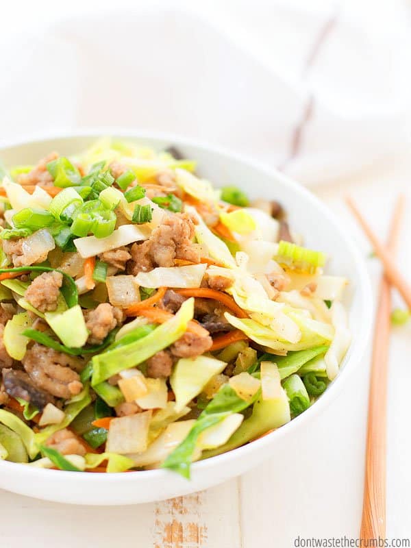 An eggroll in a bowl recipe with ground pork, sauteed cabbage, carrots and green onions. There are chop sticks on the table beside the bowl. 