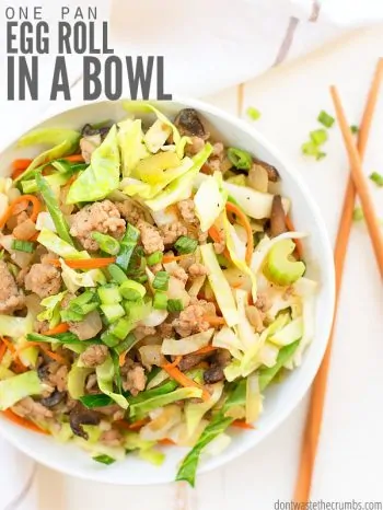 Round white dinner bowl filled with ground pork, shredded cabbage, green onions, colored with orange sliced carrots. A pair of chopsticks sit ready. Text overlay One Pan Egg Roll in a Bowl.