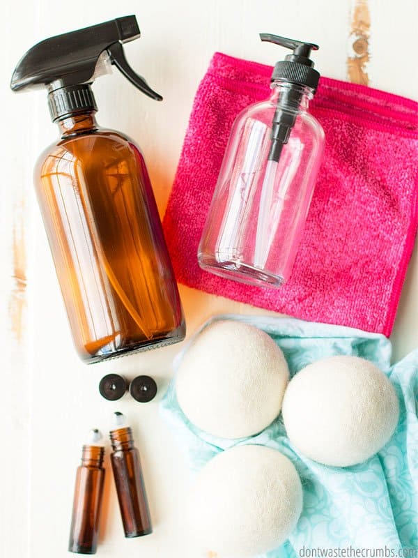 Amber glass spray bottle laying on a white cloth, glass spray bottle laying on a pink cloth, two essential oil amber glass bottles laying on a white cloth, 3 big cotton balls.