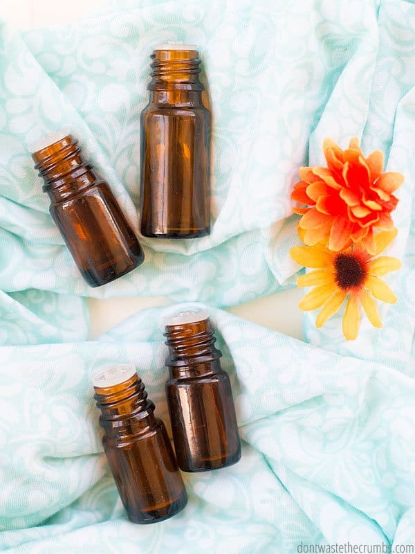 Four amber glass essential oil bottles laying on a blue cloth on table with two orange flowers