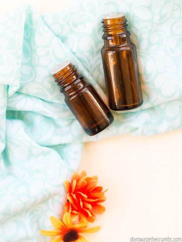 Two amber glass essential oil bottles laying on a blue cloth on a table with an orange flower.