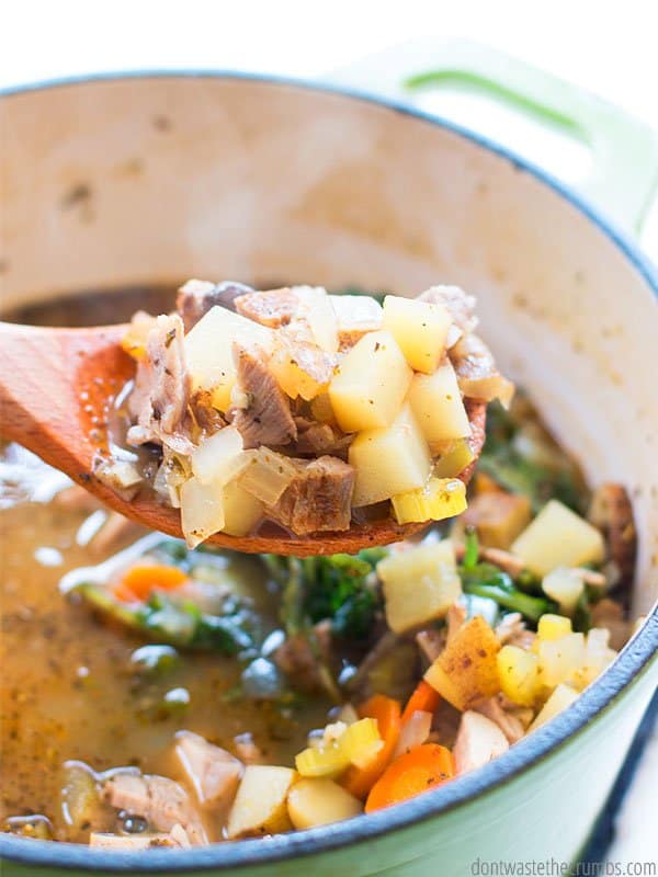 Leftover pork and potato soup in a stock pot. A close up of a spoonful of soup.