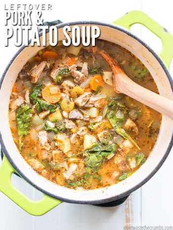 Overview of a large ceramic cooking pot, with green lime green handles and a charcoal colored rim, filled with a hearty soup - chunks of pork, sliced carrots and potatoes, and greens, plus spices all visible. Text overlay Leftover Pork & Potato Soup.