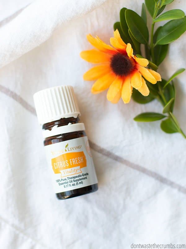 A bottle of Young Living Citrus Fresh "Vitality" oil lays on a white towel next to a yellow flower.