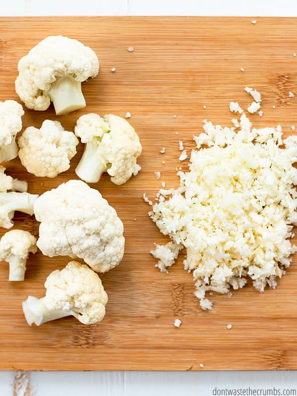 One side of the cutting board has cauliflower florets and the other side has chopped cauliflower.