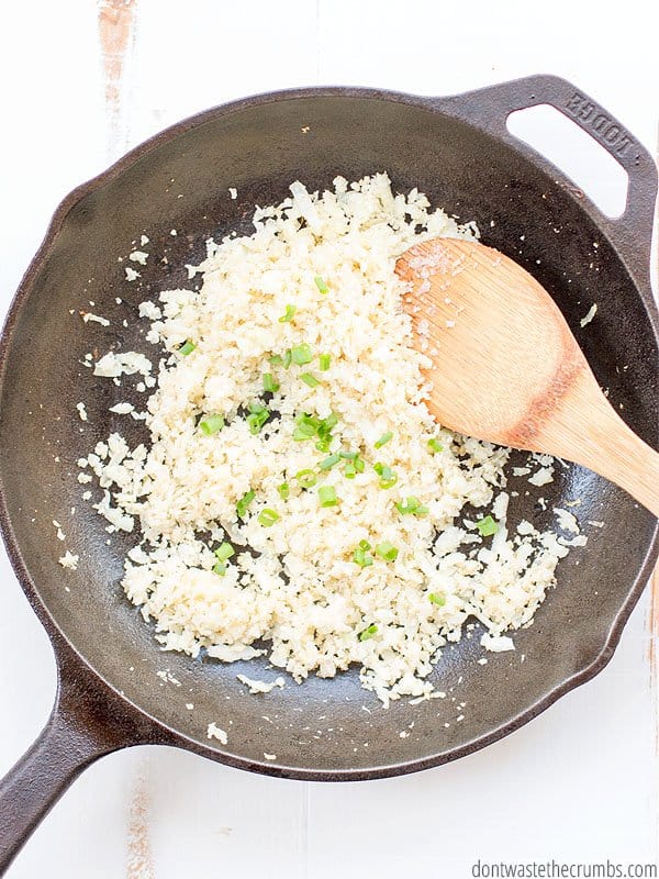Cooked cauliflower rice in a cast iron skillet with a wooden spoon.