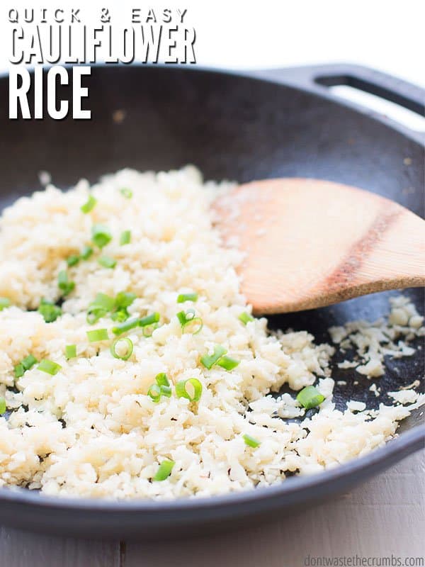 Cast iron pan filled with white rice and green onions, a wooden spatula its alongside. Text overlay Quick and Easy Cauliflower Rice.