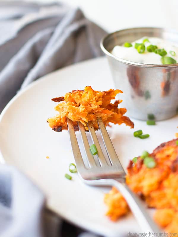 White dinner plate with four round, fried Sweet Potato fritters, one with a bit take out of it. A small dish of dipping sauce sits on the side. Text overlay Carrot Sweet Potato Fritters.