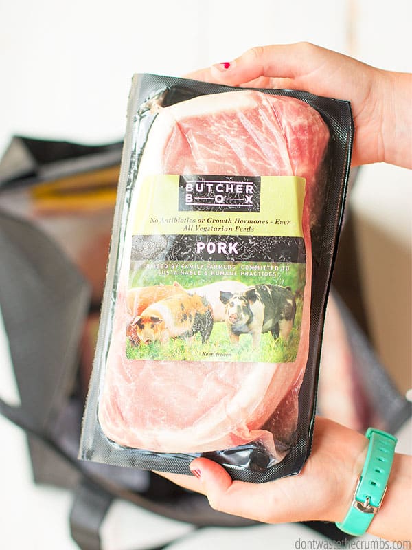 Hands holding a package of heritage pork shown in Butcher Box packaging over a white background.