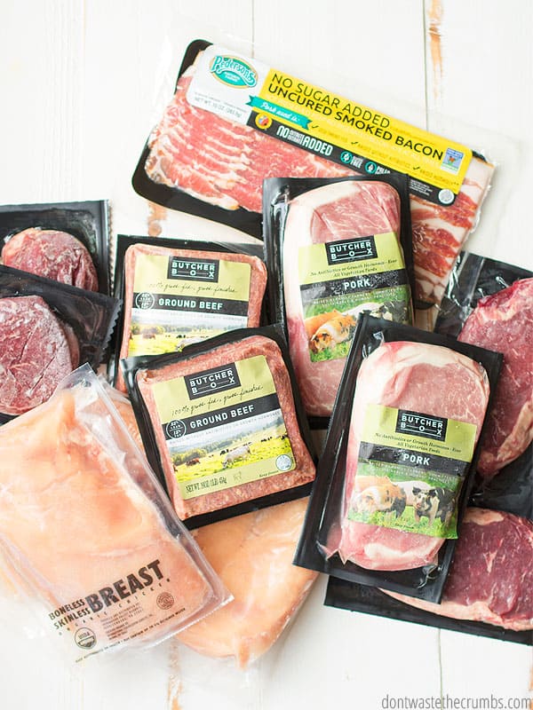 Various packages of frozen meats and chicken, all in Butcher Box packaging, on a whitewashed wooden table top. 