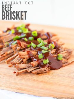 Wooden serving plank with shredded beef brisket, coated with BBQ sauces and diced green onions..Text overlay Instant Pot Beef Brisket.