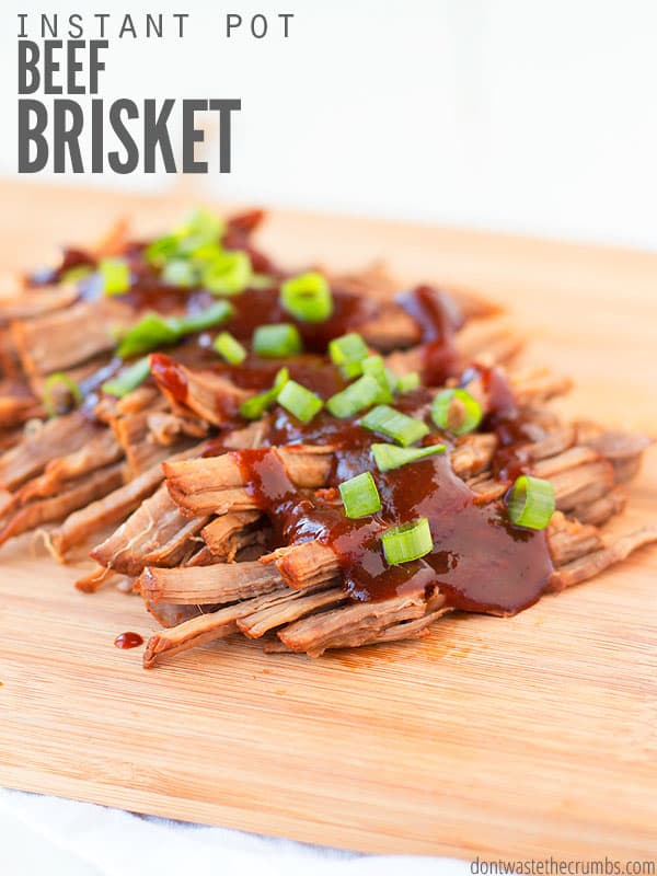 Wooden serving plank with shredded beef brisket, coated with BBQ sauces and diced green onions..Text overlay Instant Pot Beef Brisket.
