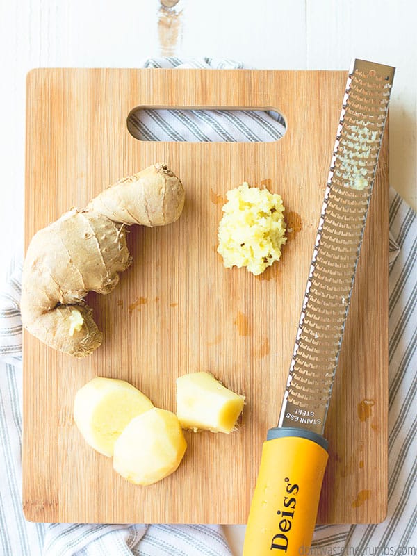 Ginger and sliced ginger and grated ginger on a wood cutting board next to a grater