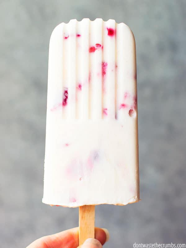 A yogurt pop with strawberries and raspberries mixed in shows the ridges of the popsicle mold.