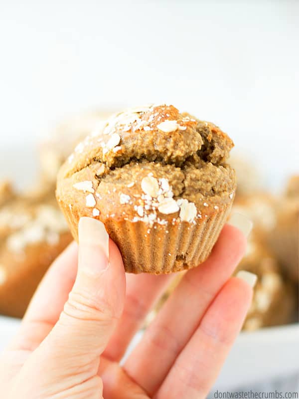 Up close view of a hand holding a banana bread muffin with a sprinkle of rolled oats on top.