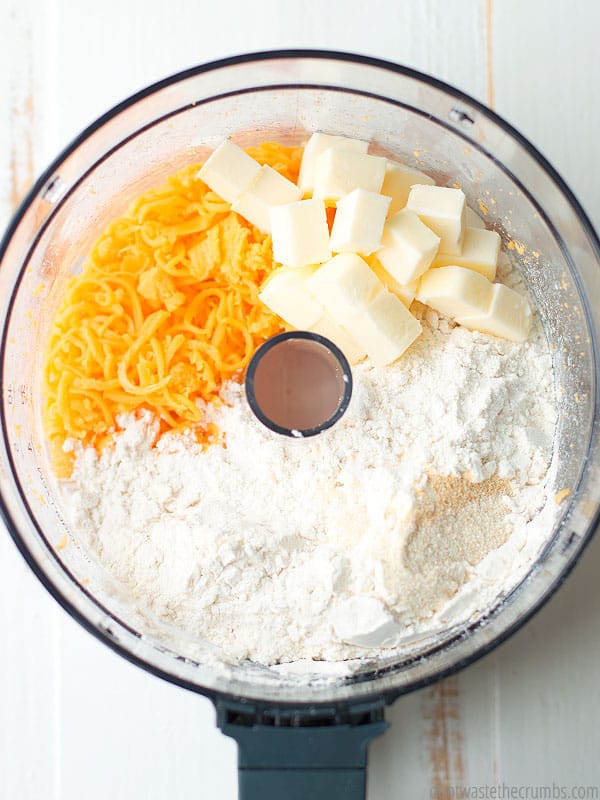 Food processor without the lid with flour, cubes of butter, and shredded cheese