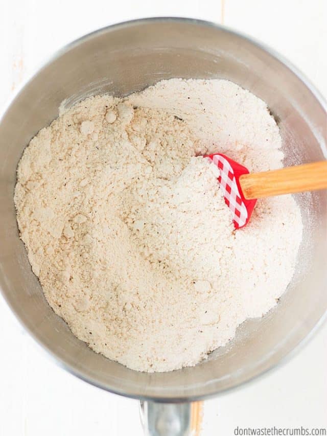 White flour being stirred in a metal bowl with a red and wood spatula.