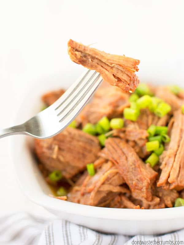 A fork holds a piece of wonderfully cooked meat above a bowl of Korean beef.