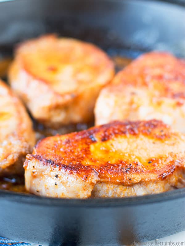 Four maple glazed pork chops frying in a cast iron skillet.