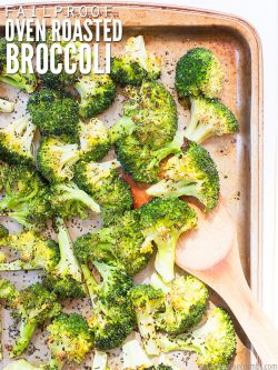 Sheet pan with roasted broccoli seasoned with herbs and a wooden spoon grabbing a scoop. Text overlay says, "Failproof Oven Roasted Broccoli".