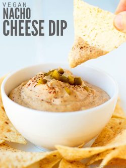 White bowl of cheese dip surrounded with tortilla chips. Text overlay Vegan Nacho Cheese Dip.