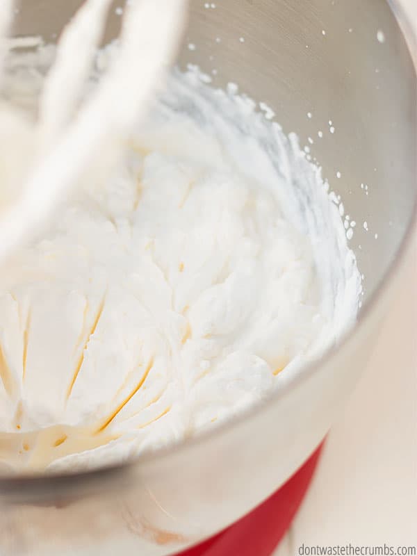 Heavy whipping cream that has been mixed to a soft peak in a red and silver mixing bowl. This whipped cream is fluffy and is a mouthwatering topping on a range of desserts!