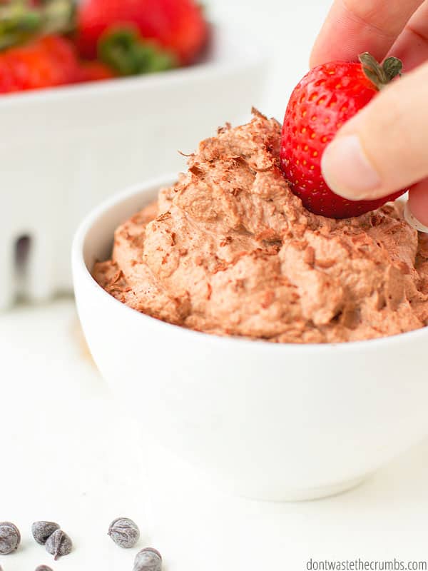 Strawberry being dipped into a bowl of chocolate whipped cream. 