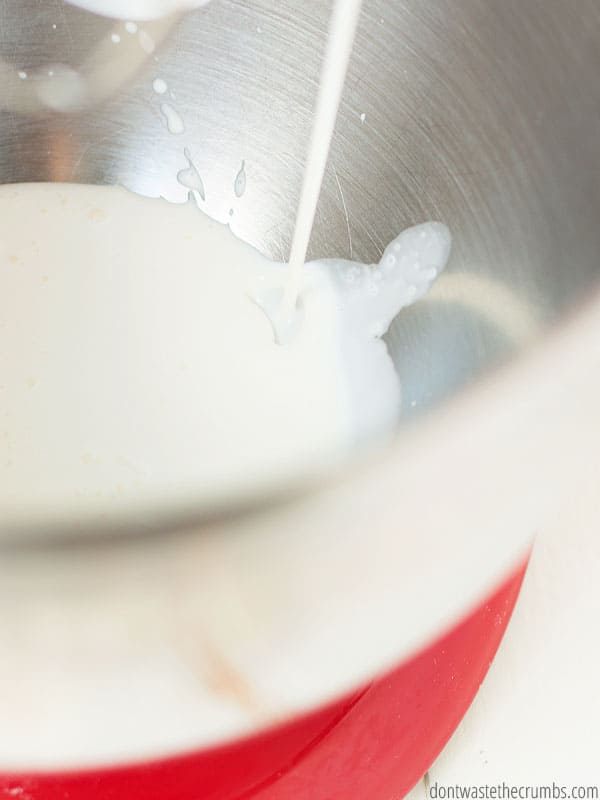 Heavy whipping cream pouring into a red and silver metal mixing bowl of a stand mixer. This homemade whipped cream is so easy to make, healthier then store bought, and delicious!