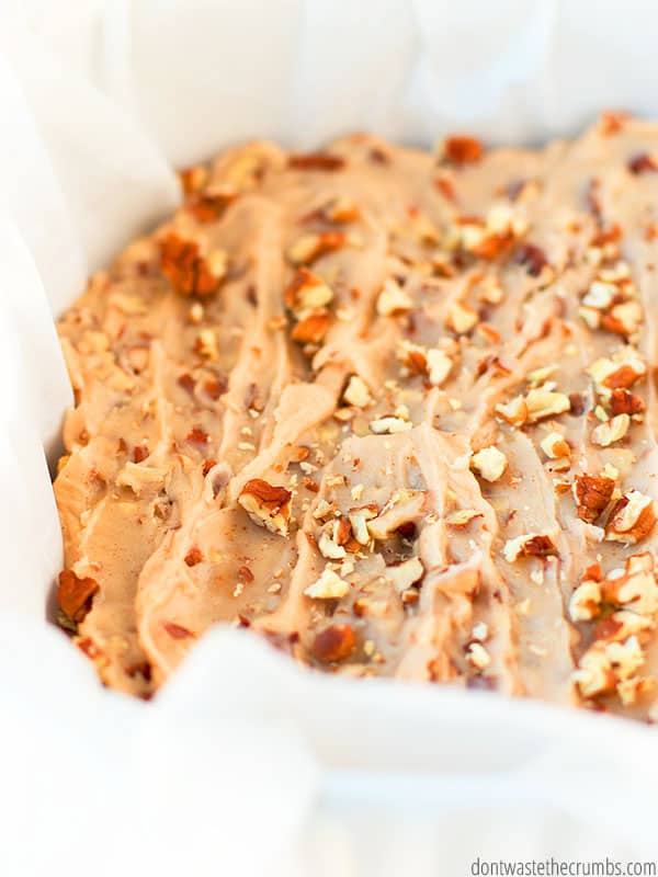 Close up of maple pecan blondies sprinkled with pecans in a pan lined with parchment paper.