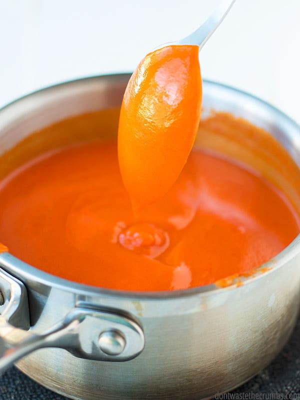 My flavorful homemade buffalo sauce in a sauce pan, being stirred with a metal spoon. 