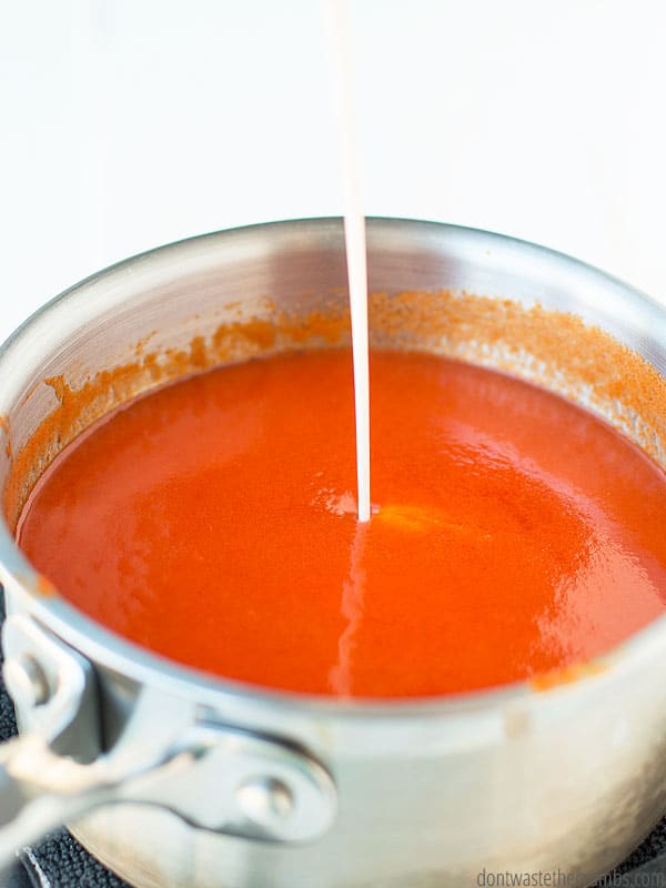 Cornstarch and water mixture is being added to the buffalo wing sauce liquid within a small saucepan. 