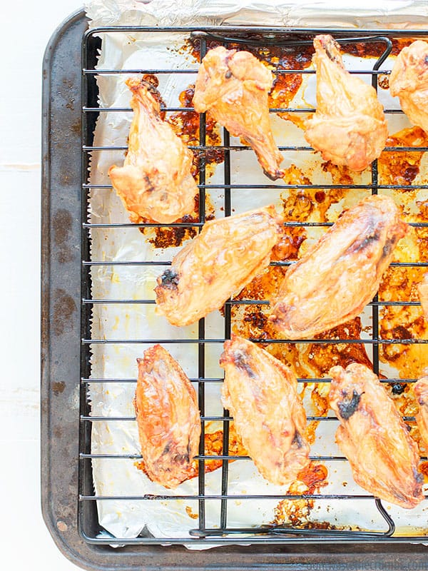 Many cooked chicken wings on a rack over a baking sheet lined with aluminum foil. You can see the crisp skin and delicious juices.